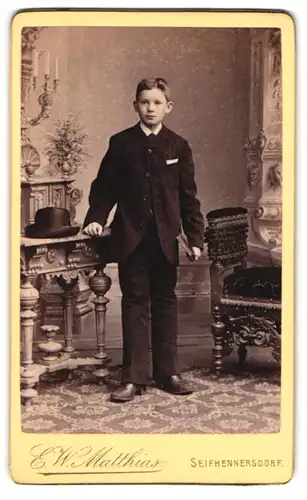 Fotografie E. W. Matthias, Seifhennersdorf, Junger Bursche trägt einen Anzug und lehnt auf einem Tisch