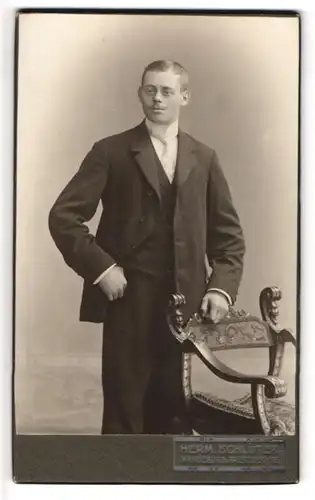Fotografie Herm. Schlüter, Magdeburg, Portrait junger Mann im Anzug neben einem Stuhl posierend