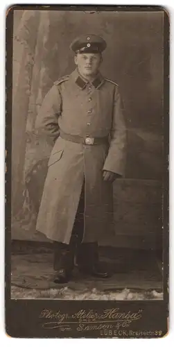 Fotografie Atelier Hansa, Lübeck, Portrait Soldat in langem Mantel eine Uniformmütze tragend