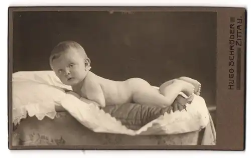 Fotografie Hugo Schröder, Zittau, Portrait nackter kleiner Bube auf einem Kissen liegend