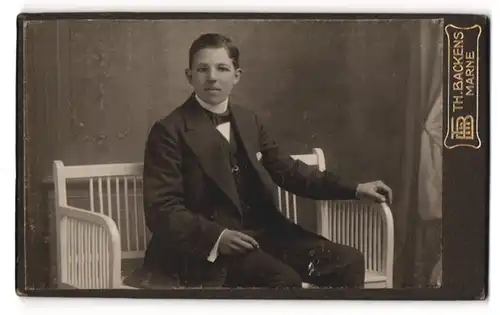 Fotografie Th. Backens, Marne, niedlicher Bube im Anzug auf einer Bank sitzend