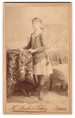 Fotografie H. Stube & Sohn, Löbau i / S., Portrait bürgerliches Mädchen mit Buch an Tisch gelehnt