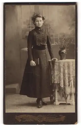 Fotografie Atelier Güttges, Zittau i. S., Portrait schönes Fräulein mit Buch an einem Tisch stehend
