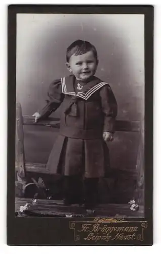 Fotografie Fr. Brüggemann, Leipzig-Neust., Portrait kleines Mädchen im Matrosenkleid auf Bank stehend