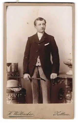Fotografie H. Walbrecker, Zittau, Portrait modisch gekleideter Herr mit Stock an Tisch gelehnt