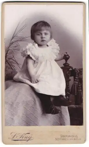 Fotografie L. Kny, Ebersbach i / S., Portrait kleines Mädchen im weissen Kleid auf Decke sitzend