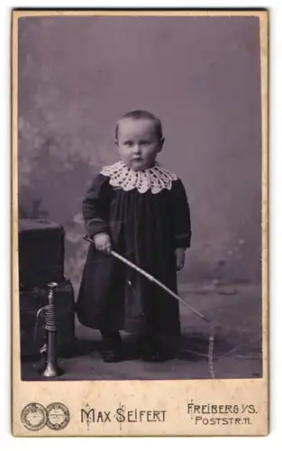 Fotografie Max Seifert, Freiberg i / S., Portrait niedliches Kleinkind im hübschen Kleid mit Peitsche