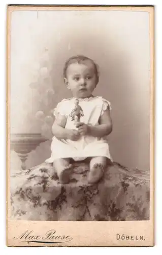 Fotografie Max Pause, Döbeln, Portrait niedliches Kleinkind im weissen Hemd mit Spielfigur auf Decke sitzend