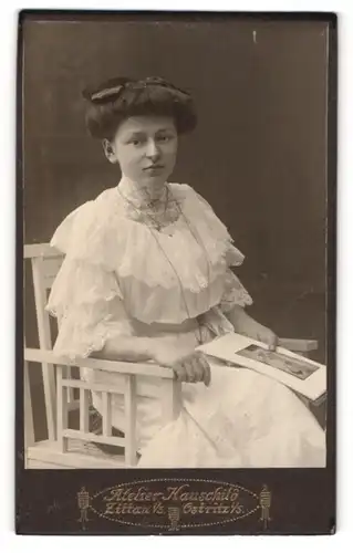 Fotografie Atelier Hauschild, Zittau i / S., Portrait sitzende Dame im weissen Kleid mit Zeitung