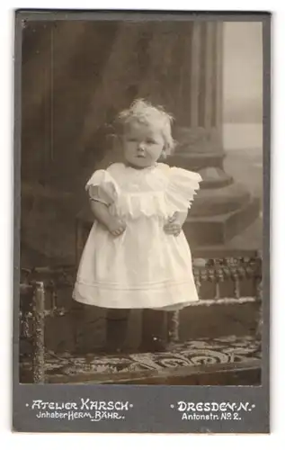 Fotografie Herm. Bähr, Dresden-N, Portrait niedliches Kleinkind im weissen Kleid auf Bank stehend