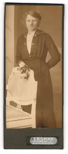 Fotografie H. Bohne, Kamenz i. S., Portrait bürgerliche Dame mit Blume an Stuhl gelehnt