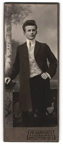 Fotografie Fr. Sartorti, Lüneburg, Portrait junger Herr in modischer Kleidung an Sockel gelehnt