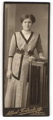 Fotografie Alfred Fritzsching, Löbau, Portrait junge Dame im karierten Kleid mit Blume an Tisch gelehnt