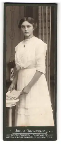 Fotografie Julius Grunewald, Oberneukirch, Portrait junge Dame im weissen Kleid mit Zeitung am Tisch