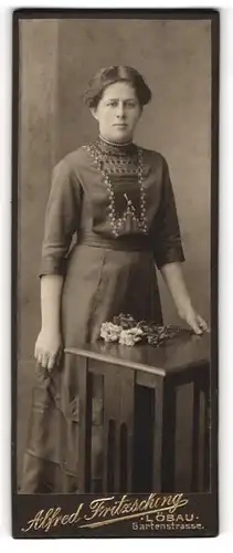Fotografie Alfred Fritzsching, Löbau, Portrait bürgerliche Dame mit Blumen an Tisch gelehnt
