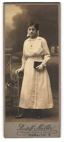 Fotografie Rudolf Müller, Görlitz, Portrait junge Dame im weissen Kleid mit Buch an Stuhl gelehnt