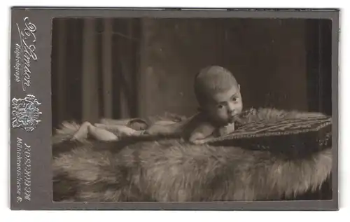 Fotografie X. Simson, Rosenheim, Portrait süsses Baby liegt auf einem Fell