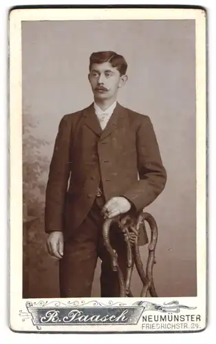 Fotografie R. Paasch, Neumünster, Portrait stattlicher Herr im Anzug an einem Stuhl stehend