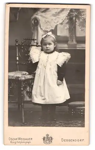 Fotografie Oscar Weidauer, Deggendorf, Portrait kleines Mädchen im hübschen Kleid an Stuhl gelehnt