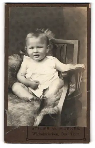 Fotografie W. Maekel, Wiebelskirchen, Portrait niedliches Kleinkind im weissen Hemd auf Fell sitzend