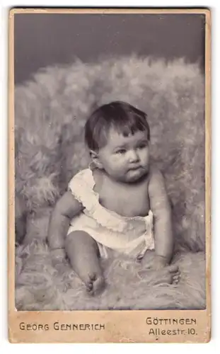 Fotografie Georg Gennerich, Göttingen, Portrait niedliches Baby im weissen Hemd auf Fell sitzend