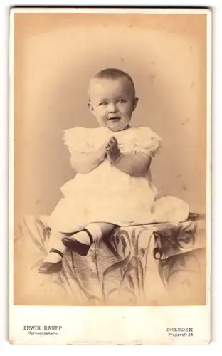 Fotografie Erwin Raupp, Dresden, Portrait niedliches Kleinkind im weissen Kleid auf Tisch sitzend