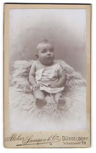 Fotografie Samson & Co., Düsseldorf, Portrait niedliches Baby im weissen Hemd auf Fell sitzend