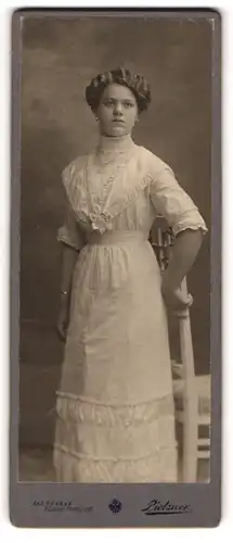 Fotografie C. Pietzner, Wien, Portrait junge Dame im weissen Kleid an Stuhl gelehnt