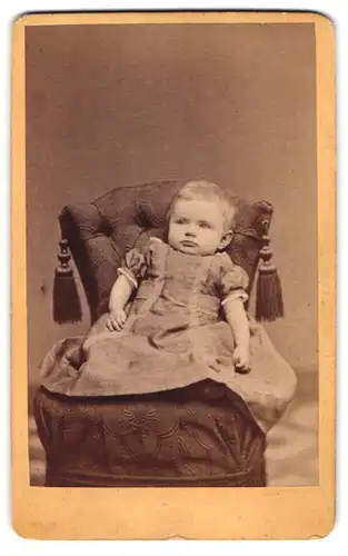 Fotografie Carl Siemsen, Hamburg-St. Georg, Portrait niedliches Kleinkind im hübschen Kleid auf Sessel sitzend