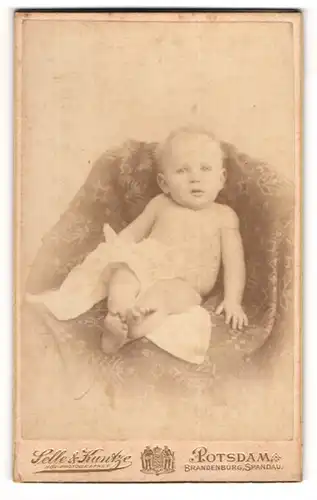 Fotografie Selle & Kuntze, Potsdam, Portrait Baby mit weissen Hemdchen auf einem Sessel posierend
