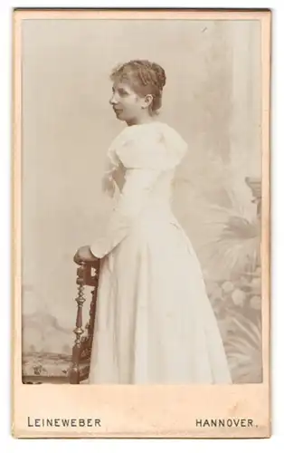 Fotografie Leineweber, Hannover, Portrait junge Dame im weissen Kleid an Stuhl gelehnt