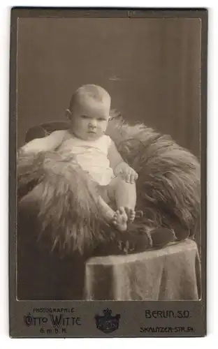 Fotografie Otto Witte, Berlin, Portrait niedliches Baby im weissen Hemdchen auf Fell sitzend