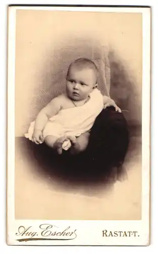 Fotografie Aug. Escher, Rastatt, Portrait niedliches Baby im weissen Hemd auf Sessel sitzend