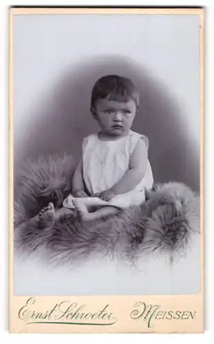Fotografie Ernst Schroeter, Meissen, Portrait niedliches Kleinkind im weissen Hemd auf Fell sitzend