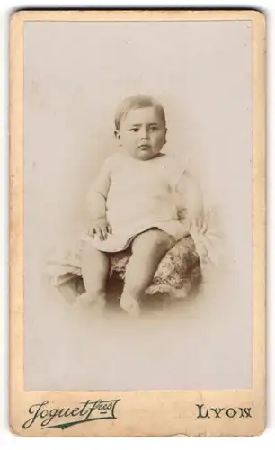 Fotografie Joguet fres, Lyon, Portrait niedliches Kleinkind im weissen Hemd auf Kissen sitzend