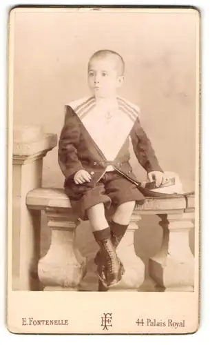 Fotografie E. Fontenelle, Paris, Portrait hübsch gekleideter Junge mit Hut auf Geländer sitzend