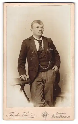 Fotografie Theodor Harder, Lunden, Portrait modisch gekleideter Herr mit Krawatte an Tisch gelehnt