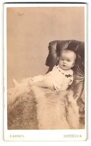 Fotografie G. Karsch, Dresden-N, Portrait niedliches Baby im hübschen Kleid auf Fell sitzend
