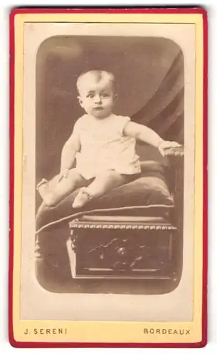 Fotografie J. Sereni, Bordeaux, Baby im weissen Oberteil sitzt auf einem Kissen