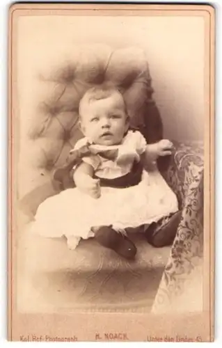 Fotografie H. Noack, Berlin, Portrait niedliches Kleinkind im weissen Kleid auf Sessel sitzend