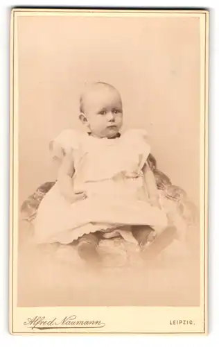 Fotografie Alfred Naumann, Leipzig, Portrait niedliches Kleinkind im weissen Kleid auf Sessel sitzend