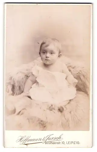 Fotografie Hoffmann & Jursch, Leipzig, Portrait niedliches Kleinkind im weissen Hemd auf Fell sitzend
