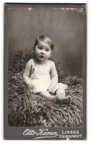 Fotografie Otto Kamm, Linden, Portrait niedliches Kleinkind im weissen Hemd auf Fell sitzend
