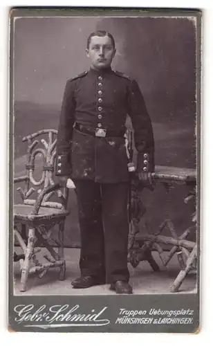 Fotografie Gebr. Schmid, Münsingen, Portrait Soldat in Uniform an Tisch gelehnt