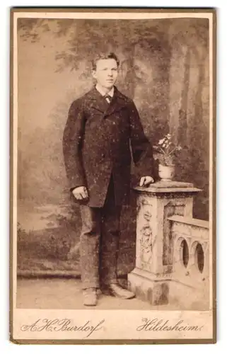 Fotografie A. H. Burdorf, Hildesheim, Portrait modisch gekleideter Mann an Sockel gelehnt