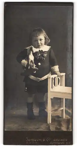 Fotografie Samson & Co., Bremen, Portrait hübsch gekleideter Junge mit Spielzeugpferd im Arm