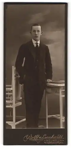Fotografie Wolff & Leonhardt, Berlin-Neukölln, Portrait junger Mann im Anzug mit Krawatte an Tisch gelehnt