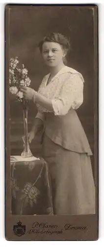 Fotografie P. Clasen, Dessau, Portrait modisch gekleidete Dame mit Blumen am Tisch stehend