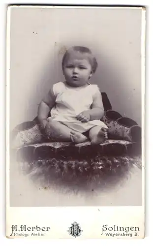 Fotografie H. Herber, Solingen, Portrait niedliches Kleinkind im weissen Hemd mit nackigen Füssen