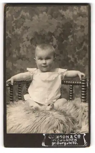Fotografie Samson & Co., Wiesbaden, Portrait niedliches Baby im weissen Hemd auf Fell sitzend